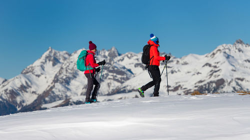 Rear view of people on snowcapped mountain against blue sky