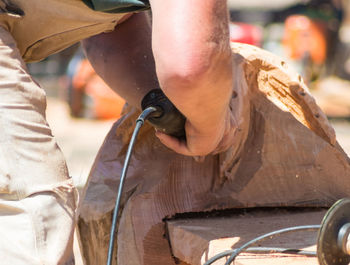 Cropped image of man using drill on wooden sculpture