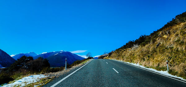 Road leading towards mountains against clear blue sky