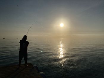 Rear view of man standing at beach against sky during sunset