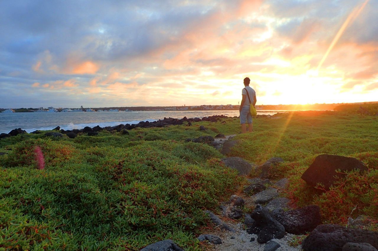 MAN STANDING ON SHORE AGAINST SUNSET SKY