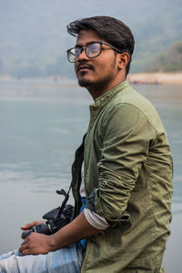 Portrait of young man wearing sunglasses standing against sea