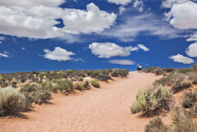 Dirt road passing through field against cloudy sky