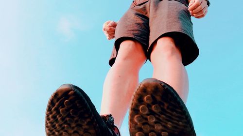 Low section of man standing against blue sky