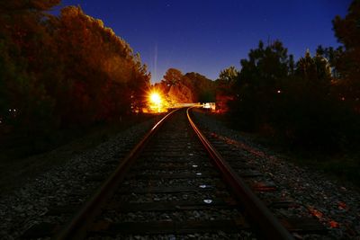 Railroad tracks amidst trees against sky at night