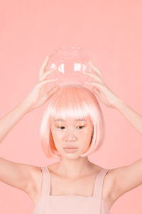 Thoughtful woman with dyed hair holding jar against wall