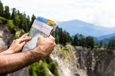 Cropped hands of people holding map against mountains