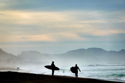 Silhouette people on beach against sky