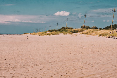 Power lines in row at sandy beach against sky