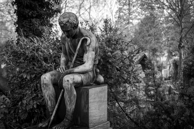 Statue of man sitting by plants