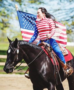 Young woman wearing american flag costume while riding horse