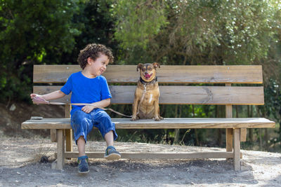 Dog and child sitting on a wooden bench in the park, the child looks at his dog 