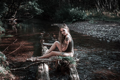 Portrait of young woman sitting in lake at forest