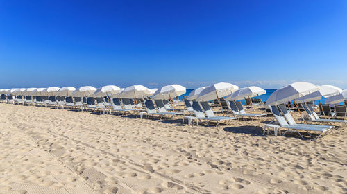 Deck chairs on beach against clear blue sky