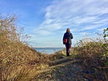 Rear view of woman walking on land against sea and sky