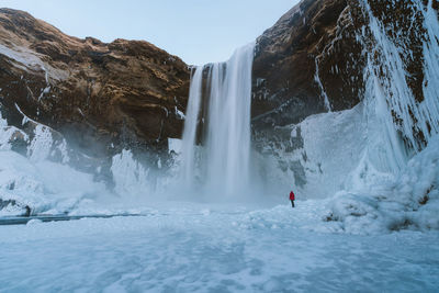 Mid distance view of man on snow by waterfall during winter