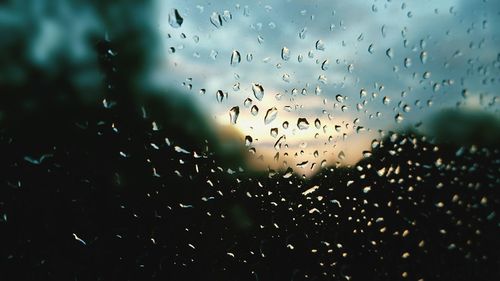 Close-up of water drops on window against sky