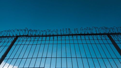 Low angle view of fence against blue sky
