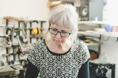 Senior woman wearing glasses while working in jewelry workshop