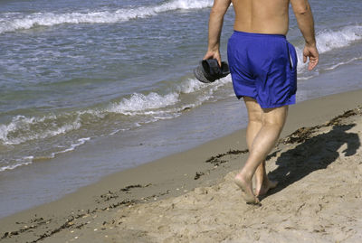 Low section of man walking on beach