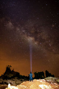 Rear view of man with illuminated flashlight standing on rock at night