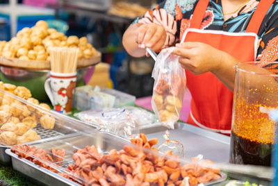 Hand holding fired meatballs put in plastic bag for sale in street food market.