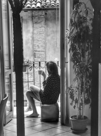 Rear view of woman looking through window at home