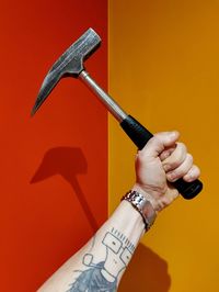 Cropped hand holding hammer against yellow background