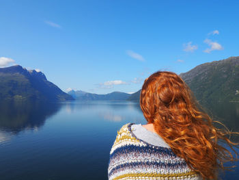 Rear view of redhead woman looking at lake against blue sky