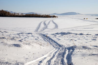 Trace from snowmobile on a snowy lake with fishermen in the background