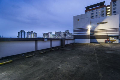 Illuminated street by buildings against sky at dusk