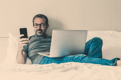 Man using mobile phone while sitting on bed at home