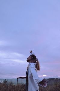 Side view of woman standing against sky during sunset