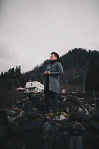 Portrait of young man standing on rock against sky