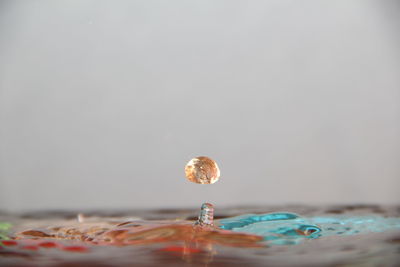 Close-up of drop falling in water against gray background