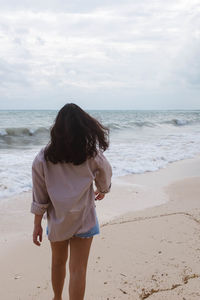 Rear view of woman walking at beach against sky