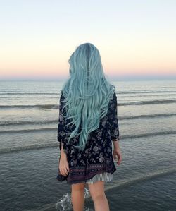 Rear view of woman with turquoise hair walking on shore at beach