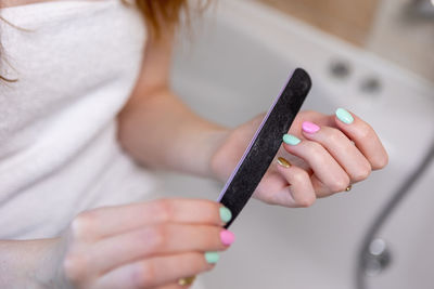 The girl makes herself a manicure sitting in the bathroom, she saws multi-colored nails with a file