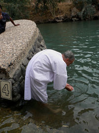 Mature man bending by rock in jordan river