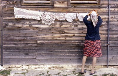 Rear view of woman drying place mats against house