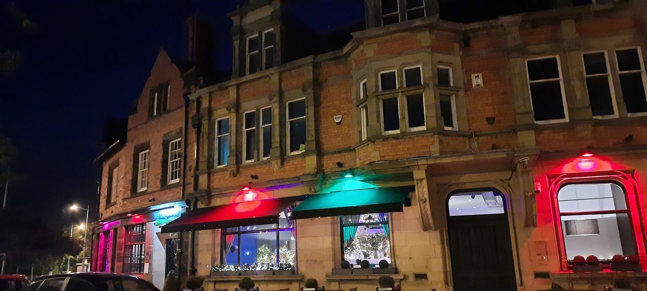 LOW ANGLE VIEW OF ILLUMINATED STREET BY BUILDINGS AT NIGHT