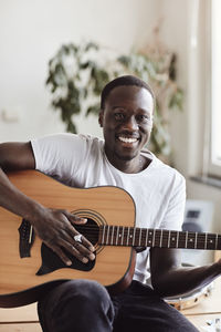 Portrait of happy young man practicing guitar while sitting in classroom