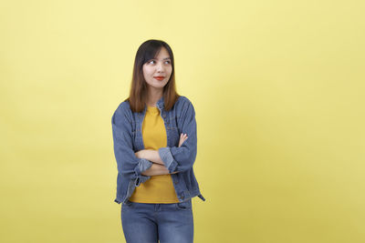Portrait of young woman standing against yellow background