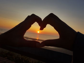 Midsection of heart shape against sky during sunset