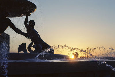 Silhouette man splashing water at beach against sky during sunset