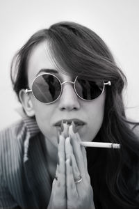 Close-up portrait of confident young woman holding cigarette against white background