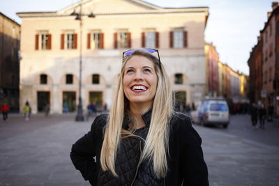 Cheerful young woman looking up while standing in city