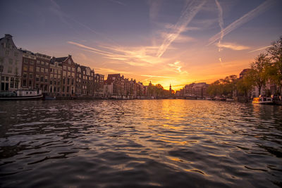 Scenic view of river by buildings against sky during sunset