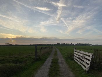 Road amidst field against sky during sunset