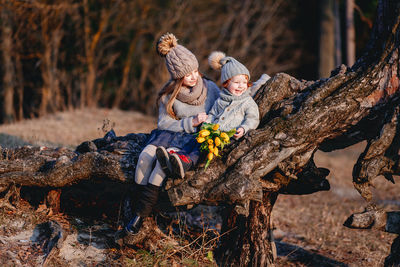 Full length of cute siblings by tree trunk outdoors